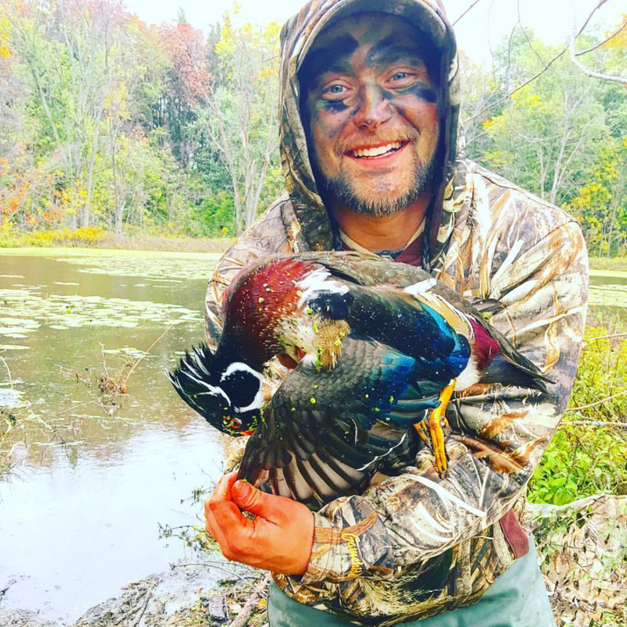Mike Hackney holding a duck outdoors in camouflage